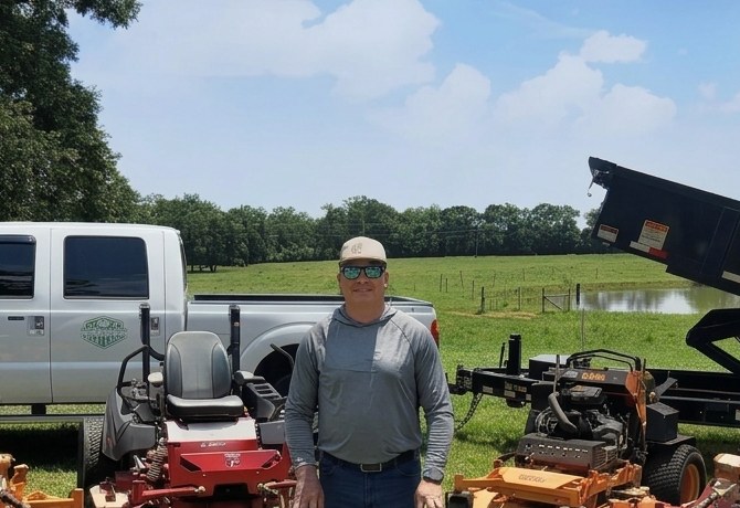 The Greener Side Solutions owner standing in front of the crew truck, mowers, and dump trailer